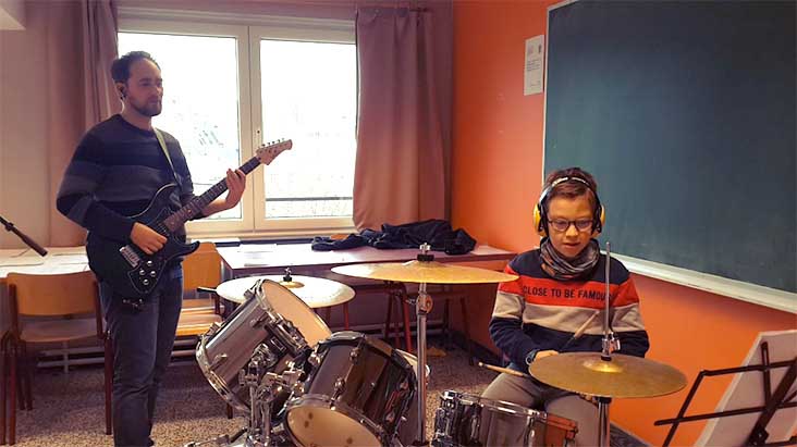 Jeune garçon en train de jour une musique à la batterie, avec son professeur à la guitare