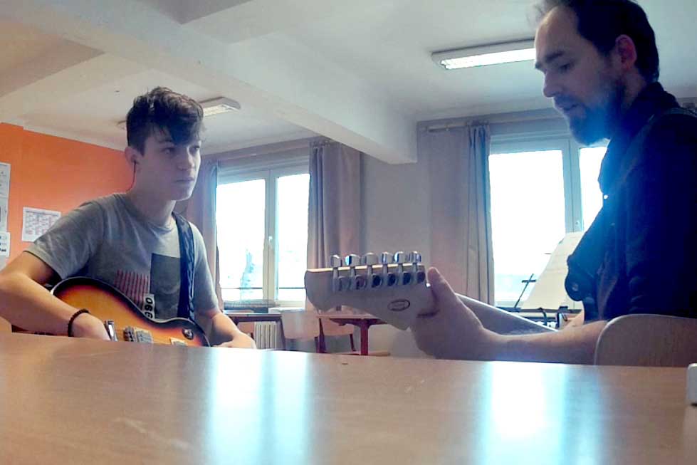 Adolescent pendant un cours de guitare, qui écoute attentivement son professeur en train de jouer