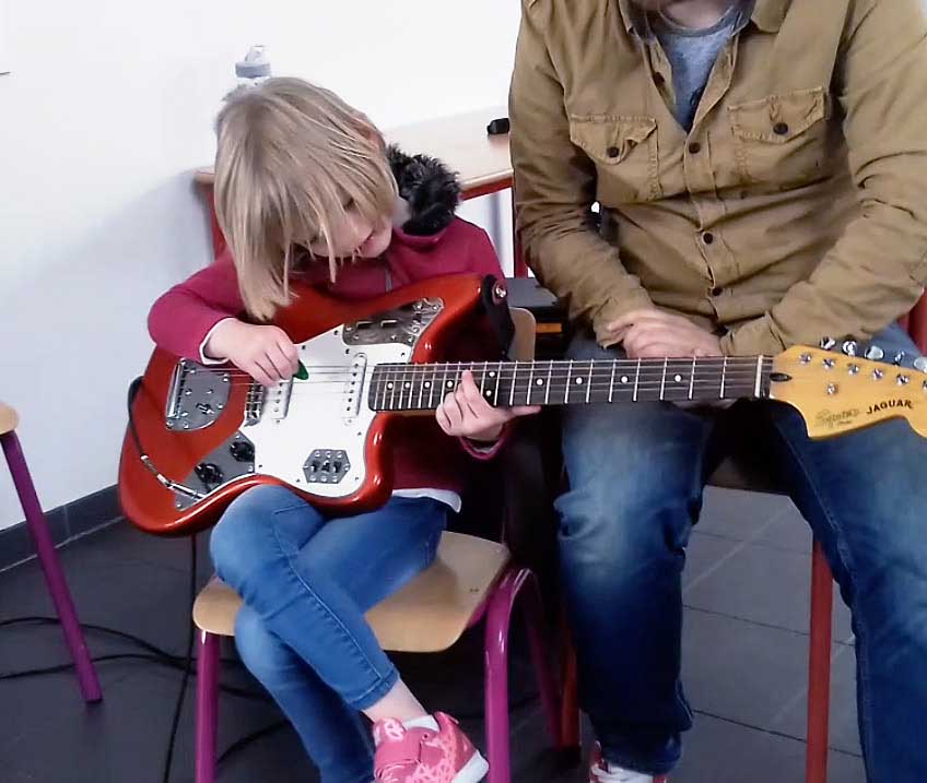 jeune fille qui joue de la guitare, aidée de son professeur de guitare